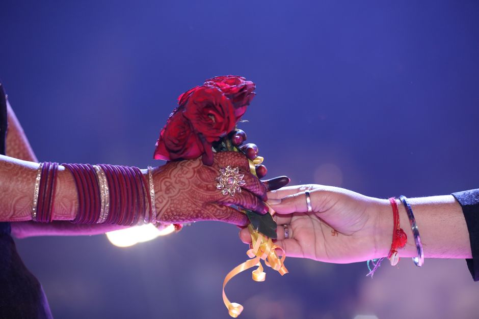 Close-up of an Indian wedding hand exchange with red roses and henna decorations, symbolizing love.